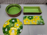 Four ceramic serving and planter pieces including a round covered dish with floral lid, a rectangular tray with floral pattern, a rectangular planter with green glaze inside, and a plain round planter.
