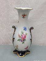 Front view of the white porcelain vase showing colorful floral decoration, cobalt blue base and handles with gold trim and detailing.