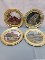 Four vintage round solid brass plates with foil print pictures showing English countryside and cottage scenes.