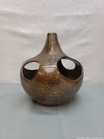 Front view of a brown speckled ceramic piece with multiple oval openings, showing its bulbous round base and narrow neck.