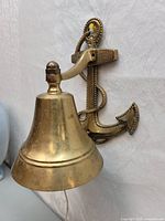 Side view showing the brass bell hanging from the anchor-shaped backplate with rope detailing and pull cord visible.