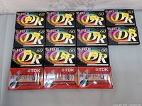 Twelve sealed cassette tapes stacked in two rows, nine Fuji DR 60-minute tapes on top and three TDK Superior 90-minute tapes on bottom.