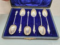 Set of six Apostle spoons in blue velvet lined case showing twisted handles, Apostle figure tops and scalloped spoon bowls.