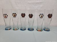 Front view of all six Moosehead beer pilsner glasses in a row showing different Manitoba Moose hockey jersey logos.