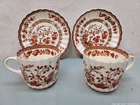 Two sets of Copeland Spode India Tree teacups and saucers side by side on a surface, showing front and patterned sides.
