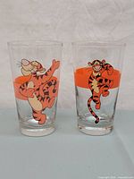 Pair of vintage Disney Tigger drinking glasses showing different Tigger illustrations and the orange band design on each glass.