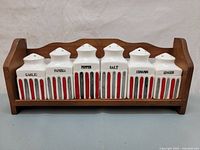 Front view of wooden spice rack with six ceramic spice jars lined up, clearly showing labels and decorative stripes.