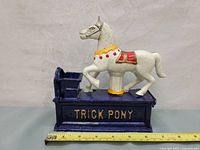 Front view of vintage cast iron Trick Pony mechanical coin bank showing white horse on a blue base with 'TRICK PONY' printed on front