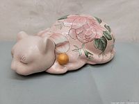 Front and side view of the vintage Webi sleeping cat porcelain figurine showing the floral hand paint and the golden bell detail.