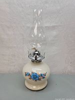Full view of the vintage white glass oil lamp with clear chimney and blue floral decorative pattern on base.