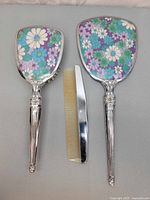 Front view of hand mirror, hairbrush, and comb showing floral design backs and silver-toned handles