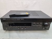 Front angled view showing Yamaha RX-V393 AV receiver with remote resting on top, showcasing the buttons and dial interface.