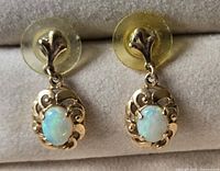 Pair of gold earrings featuring oval opal stones set in decorative gold frames with post backs and clear plastic backings.