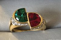 Top angled view of gold plated ring showing large green and red half-moon shaped stones and small clear stones on sides.