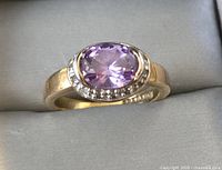 Photo showing the front face of the ring with central oval purple faceted stone and small clear accent stones around it on a gold plated band.