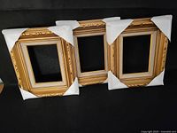 Photo showing the three carved wooden photo frames grouped side by side with protective corner covers on each frame.