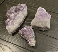 Photo of three amethyst crystal pieces on a dark wood surface showing purple hues and crystalline structure.