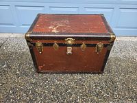 Front view of the antique steamer trunk showing brass hardware and leather handles