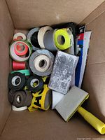 Box filled with multiple rolls of tape in different colors and sizes along with sanding blocks and sponges