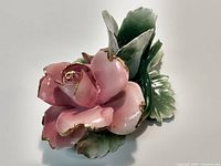 Close-up of a ceramic pink rose with gold edges and green leaves, showing detail and craftsmanship.