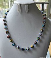 Full view of colourful glass bead necklace displayed on a white mannequin bust, showing the bead pattern and length.