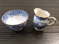 Photo showing blue and white cream pitcher and matching sugar bowl with gold trim on rims and handles against black surface