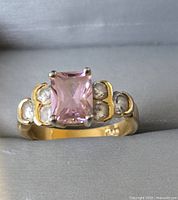 Front view of fashion ring showing pink rectangular gemstone center and clear accent stones on gold-tone band.