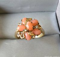 Close-up front view of the ring showing coral-colored oval stones, clear stones, and gold leaf accents.