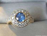 Front close-up showing blue center stone surrounded by clear stones in halo setting on gold tone band