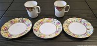 Photo of 2 Royal Albert Old Country Roses coffee mugs and 3 matching vintage lunch plates displayed on table showing floral rose pattern with gold trim.