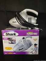 Shark Compact TurboVac handheld vacuum placed on top of its original box. Vacuum cord wrapped around handle.