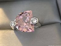 Front view of sterling silver ring showing large asymmetrical pink faceted gemstone center with two small round clear gemstones on sides