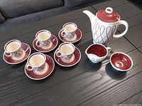 Full set shown on table, includes pot, 5 cups with saucers, creamer, and sugar bowl showing pattern and colors