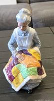Front view of the porcelain figurine showing elderly woman holding colorful patchwork quilt.