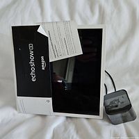 Front view of the Amazon Echo Show 5 with screen and partially visible documentation and power cable.