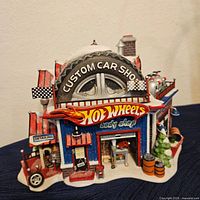 Front view showing the Custom Car Shop tire, Hot Wheels signage, detailing sign, garage door, and snow effect on roof and base.