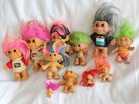 Lot of 12 vintage troll dolls laid out on white background showing various sizes, hair colors, and outfits.