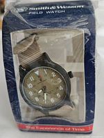 Front view of the Smith & Wesson Field Watch in its original packaging, showing the watch face and tan nylon strap.