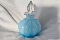 Front angle view of the vintage Fenton blue glass perfume bottle showing the scalloped body and clear topper with a ruffled collar and flame-shaped finial.