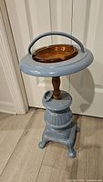 View of the full vintage smoking stand showing blue metal base, wooden post, and amber glass ashtray insert with handle.