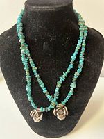 Two American turquoise beaded necklaces displayed on black bust stand, showing blue-green irregular gemstone beads and silver rose pendants.