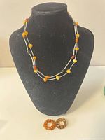 Photo showing double-strand Baltic amber necklace on black display bust with amber beaded wraparound rings placed below.