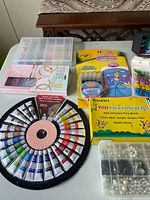 Overview of arts and crafts supplies including acrylic paints, glitter glue, pony beads, bead storage cases, and elastic string on table