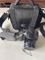 Canon PowerShot SX30 IS camera with battery charger and Lowepro carrying case on a surface.