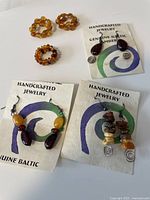 Photo showing the complete set of handcrafted Baltic amber jewelry including two pairs of drop style earrings and three rings displayed on cards.