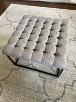 Top view showing tufted fabric upholstery and metal base on a carpeted floor.