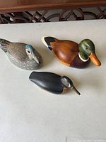 Three handcrafted wooden duck decoys arranged together on a light surface, showing different species and paint details.