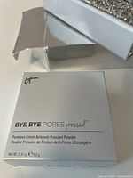 White box packaging for IT Cosmetics Bye Bye Pores translucent pressed finishing powder, text visible indicating product details and weight.