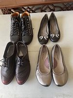 Four pairs of women's leather shoes displaying different styles including flats and lace-up casuals on a white surface.