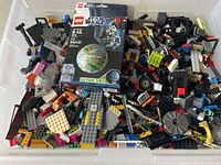 Top view of a plastic bin filled with thousands of assorted used LEGO bricks and parts including a LEGO Star Wars Series 2 set box (75187) on top.